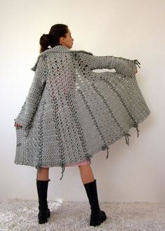 a woman is standing in front of a wall wearing a crocheted coat