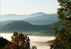 the mountains are covered in fog and mist as seen from an overlook point on a sunny day