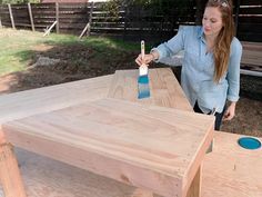 a woman is painting the top of a table with a blue paintbrush on it