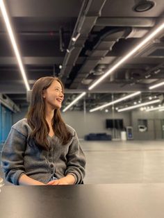 a woman sitting at a table in an empty room with bright lights on the ceiling