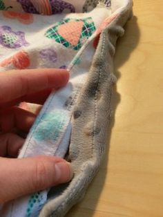 someone is sewing something on top of a cloth covered in flowers and leaves, with their fingers touching the fabric