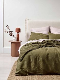 a bed with green linens and pillows in a white room next to a table