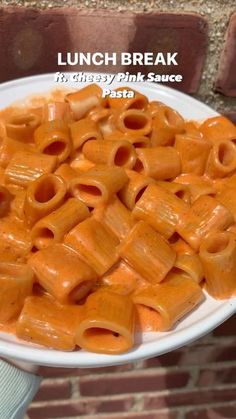 a white plate topped with pasta covered in sauce next to a brick wall and person holding it