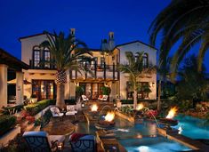 an outdoor fire pit in front of a large house with palm trees and lawn chairs