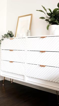 a white dresser sitting on top of a wooden floor next to a potted plant