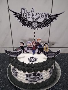 a white cake with black icing and some people on it, sitting in front of a sign