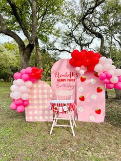 a pink and white chair sitting in front of a heart shaped sign with balloons attached to it