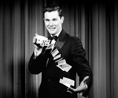 a man in a tuxedo is holding a dice and playing cards with his right hand