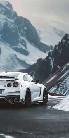 the white sports car is driving down the road in front of snow covered mountain peaks