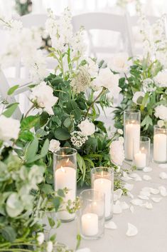 white flowers and greenery are arranged on the table for a wedding reception with candles