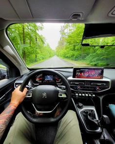 a man driving a car on a road with trees in the background