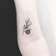 a black and white photo of a flower tattoo on the left inner arm, with a ball of yarn behind it