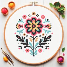 a cross - stitch pattern with flowers and leaves on the table next to some knitting needles