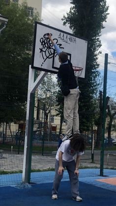 two people are playing basketball on a court in front of a fenced area with blue tarps