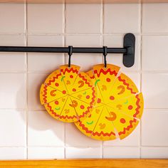 two paper pizza slices hanging from a black rack on a white tiled wall above a wooden counter