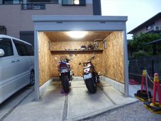 two motorcycles are parked in the back of a small garage with its doors open to let people inside