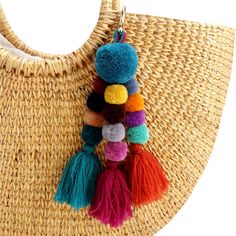 multicolored tasselled pom - pom keychain hanging from woven straw bag