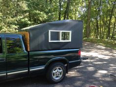 a green truck with a small house on the back and windows in it's bed