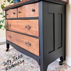 an old dresser is painted black and has knobs on the drawers, with a plant in the corner