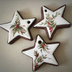 three decorated cookies in the shape of stars with holly and berries on them, sitting on a table