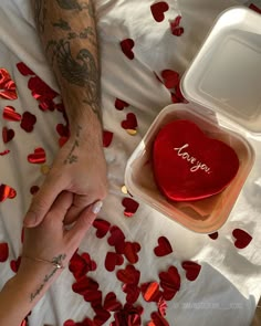 two people holding hands over a heart shaped cake in a box with the word i love you written on it