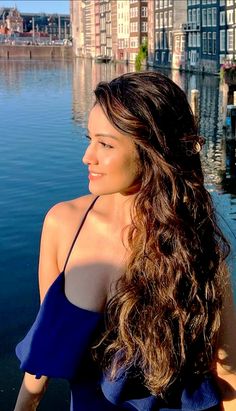 a woman with long hair standing next to the water