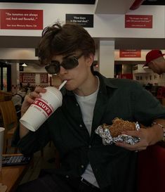 a man sitting in a chair drinking from a cup while holding a donut and a drink