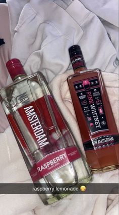 two bottles of alcohol sitting next to each other on a bed with white sheets and blankets