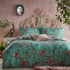 a bed with pink and blue flowers on it in a room next to a potted plant