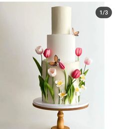 a three tiered cake with flowers and butterflies on the top is decorated in white icing