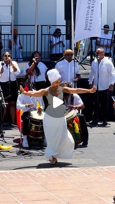 a woman in a white dress is dancing on the street with other people behind her