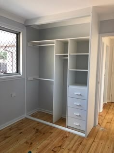 an empty room with white shelves and drawers in the corner, next to a window