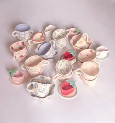 a collection of tea cups and saucers with strawberries in them on a white surface