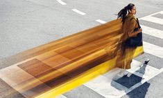 a woman walking across a cross walk holding onto a wooden bench