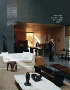 a man standing in a living room next to a white couch and coffee table with vases on it