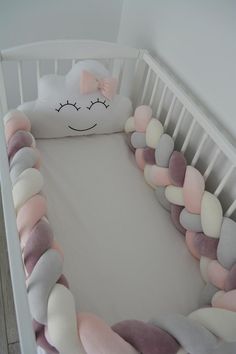 a white crib with a pink and grey pillow in the shape of a cloud