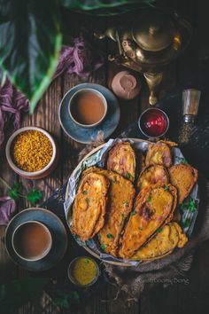 some food is sitting on a table next to cups and sauces