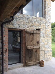 an open wooden door in front of a stone building with glass doors and brick walls