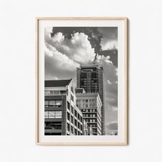 a black and white photo of buildings with clouds in the sky above them, framed in wood frame