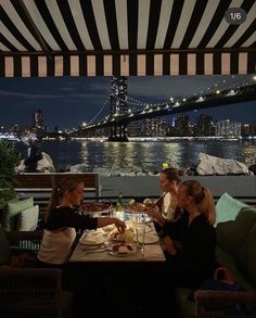 three women sitting at a table with food in front of the brooklyn bridge