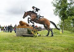 a person on a horse jumping over a brick structure in the grass with people watching