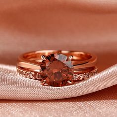 two rose gold wedding rings with an orange diamond in the center on a pink cloth