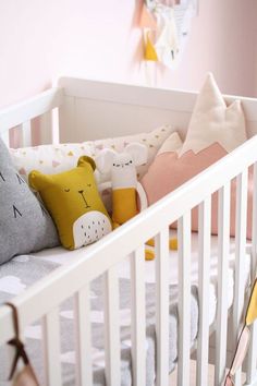 a white crib with stuffed animals and pillows on it's sides in a pink nursery