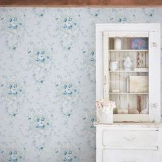 a white cabinet with blue flowers on it next to a wallpapered wall in a room