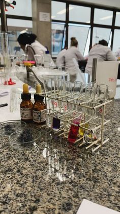 several wine glasses and bottles on a counter top with people in the background at work