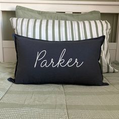 a black pillow with the word parker on it sitting on top of a white bed