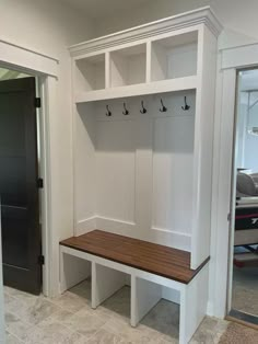 a white mud room with two benches and coat hooks on the wall, along with an open door