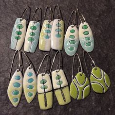 nine pairs of earrings with green and white designs are on a black surface, one is hanging from the earwires