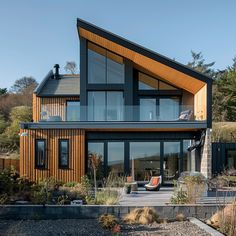 a modern house with large windows and wooden sidings on the roof, along with an outdoor seating area