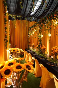 an indoor event with sunflowers and greenery on the walls, black table cloth draped in yellow